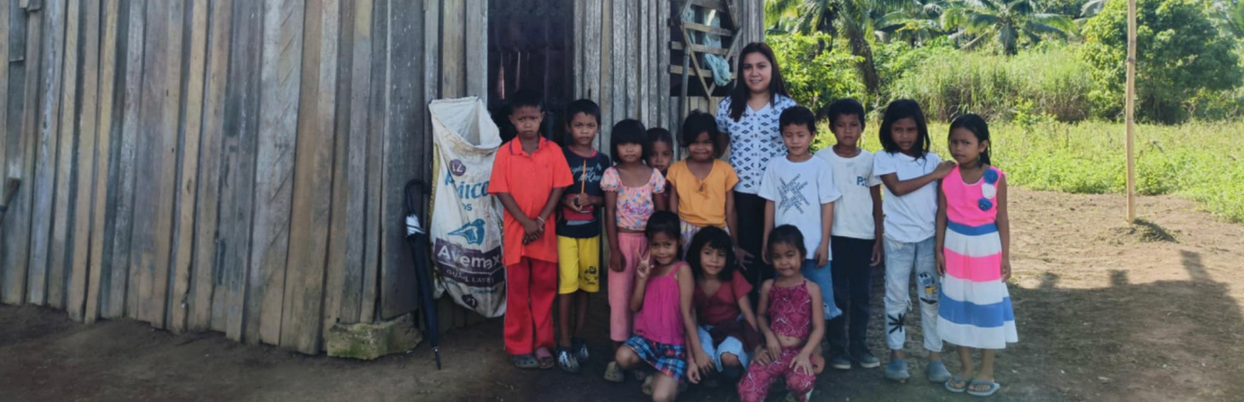 A group of children and an adult woman standing outside a rustic wooden house