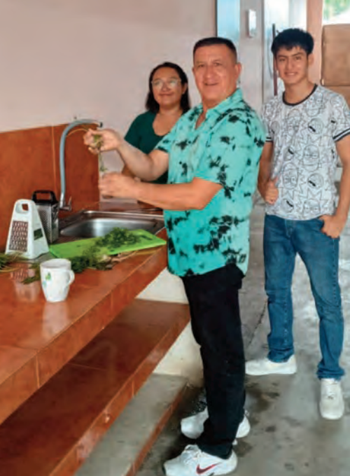 One adult gentleman and two younger adults preparing vegetables in a kitchen in Ecuador