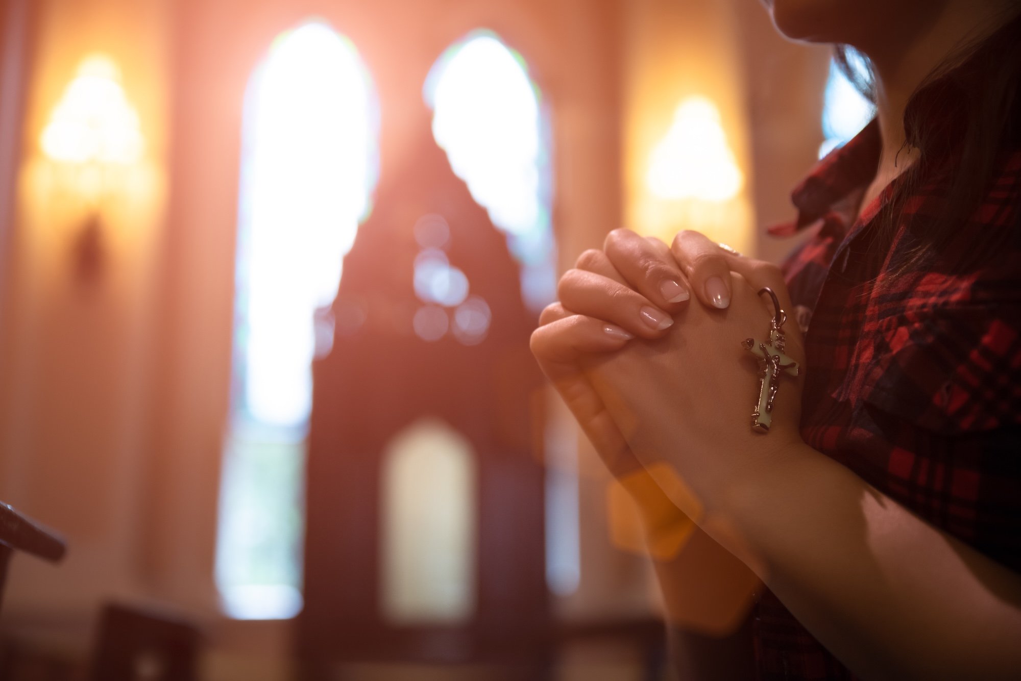 Woman hand holding rosary against cross and praying to God at church